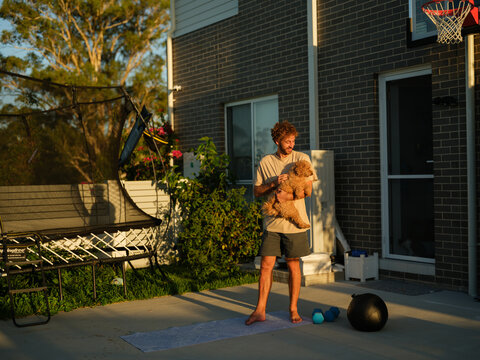 Man stands on a mat holding a dog while working out