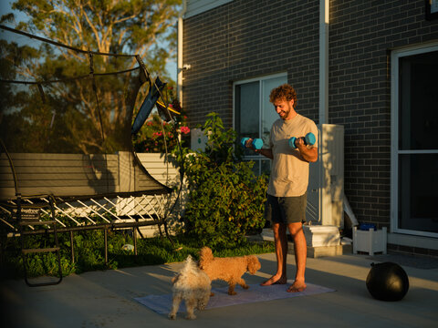Man doing a bicep curls with dumbbells beside two dogs in the backyard