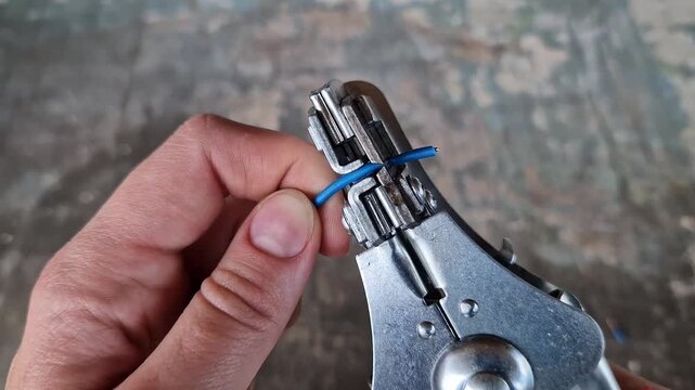 The process of stripping insulation from a blue wire using an automatic stripper. Hands of a craftsman using a professional pliers tool to remove the insulation from a copper electrical cable