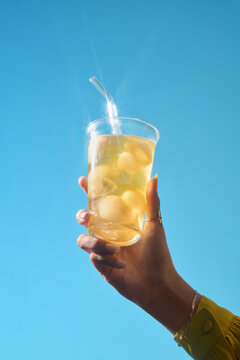 A hand holds a glass of refreshing iced tea against blue sky