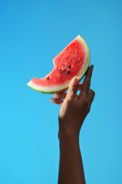 A hand holds a delicious slice of watermelon against a bright blue sky