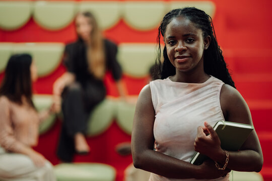 Young black student holding a book, standing in a vibrant modern university lounge, learning and diverse education concept