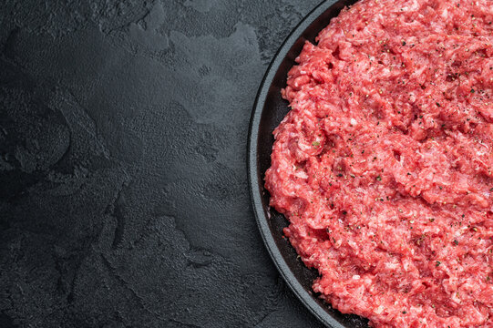 Uncooked minced veal or beef meat on round black dish with spices highlighting raw texture perfect for culinary and food preparation visuals.
