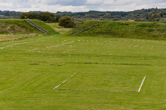 View of the Viking Museum Fyrkat with white markings outlining ancient house foundations on a grassy field surrounded by earthen ramparts in Hobro, Jutland, Denmark.
