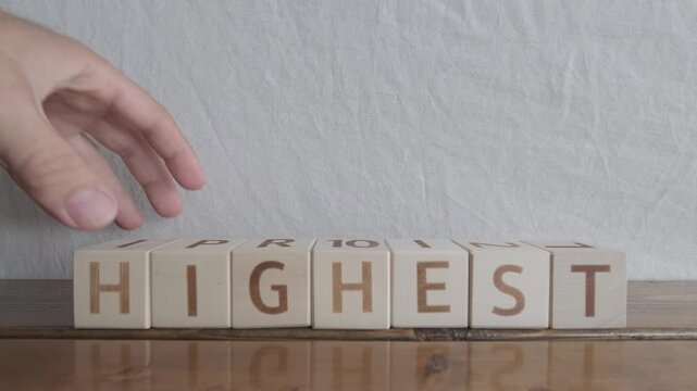 motivational word Highest, laying out by hand from letters on wooden cubes, slow motion

