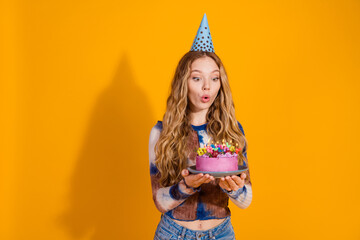 Young girl celebrates birthday with pink cake and candles against bright orange background in a...