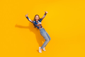 Fototapeta premium Young woman in casual outfit jumps with joy against a bright yellow background for lifestyle fashion advertising and promotion