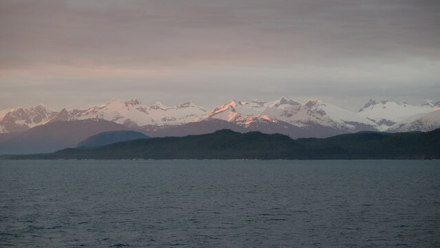 Breathtaking Alaska mountain glacier range view seen from outdoor deck of cruise ship liner sailing the Inside Passage transit with spectacular landscape scenery during sunset