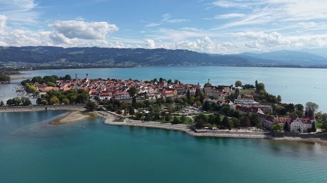 Aerial panoramic view of Lindau Island on Lake Constance in Bavaria, Germany, with the historic old town, marina, waterfront and green Alpine foothills under a dramatic summer sky.