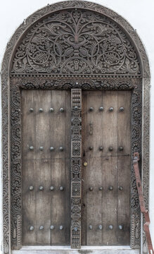 View of a traditional intricately carved wooden door with brass studs and an arched frame in Zanzibar, Mjini Magharibi Regio, Tanzania.