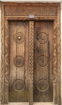 View of a traditional intricately carved wooden door with circular floral motifs and metal studs in Stone Town, Zanzibar, Mjini Magharibi Regio, Tanzania.