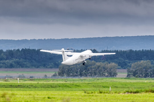White passenger turboprop airplane takes off runway in cloudy weather