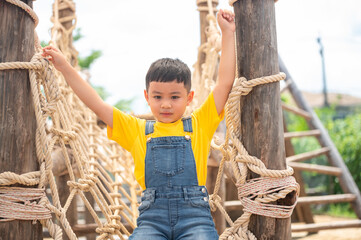 A joyful child in a bright yellow shirt climbs a rope structure, showcasing the joy of play and...