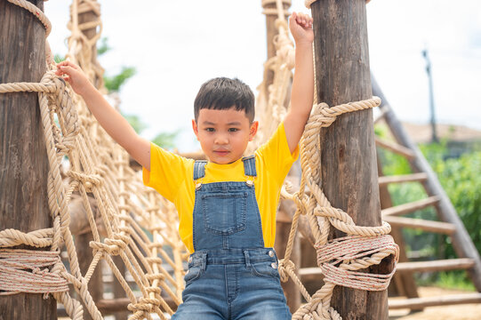 A joyful child in a bright yellow shirt climbs a rope structure, showcasing the joy of play and outdoor adventure. Perfect for capturing childhood happiness.