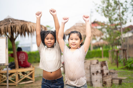 Two joyful children raising their hands in celebration outdoors, embodying friendship and happiness in a vibrant community setting.