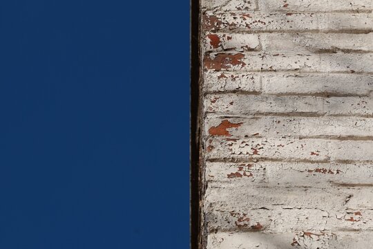Peeling white paint on an old brick wall against a deep blue sky with large copy space