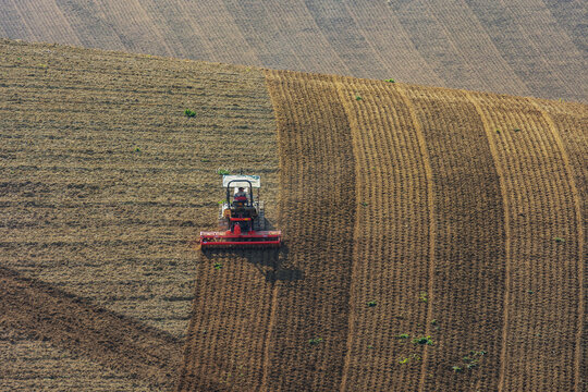 View of a tractor plowing a field on rolling hills in Corridonia, Marche, Italy.