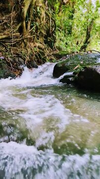 Vertical 9:16 4K footage of fast-flowing water rushing between natural rocks in a stream. The water strikes the stones and creates visible splashes, capturing detailed movement in a refreshing natural