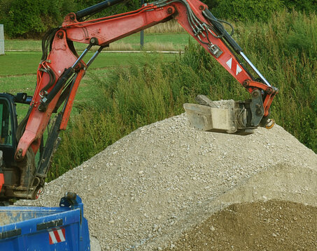 View of an excavator arm with a hydraulic attachment working on a large pile of gravel at a construction site in Garching, Bavaria, Germany.