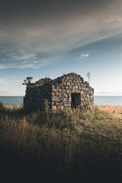 View of an old stone ruin situated on the grassy coastline by the sea under a dramatic cloudy sky in Virtsu, Parnu maakond, Estonia.