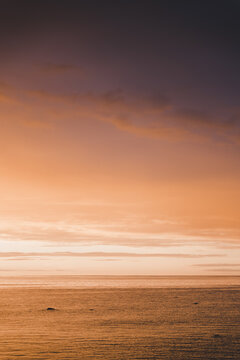 View of the calm sea during a vibrant sunset with warm orange and purple hues reflecting on the water in Merikula, Harju maakond, Estonia.