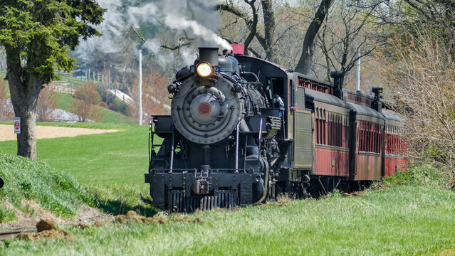 View of a historic steam locomotive pulling vintage passenger cars through the lush green countryside in Ronks, Pennsylvania, United States.