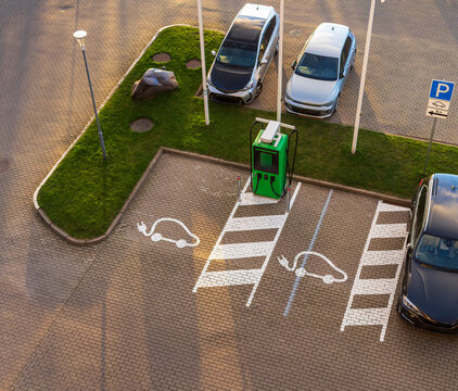 View of an electric vehicle charging station in a parking lot with painted EV symbols on the pavement and cars parked nearby in Klaipeda, Klaipeda County, Lithuania.