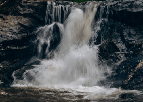 View of a cascading waterfall flowing over dark rocky cliffs in the natural landscape of Jos East, Plateau, Nigeria.