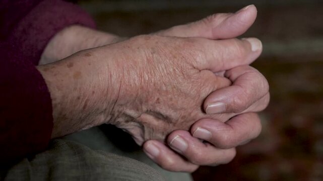 Closeup view elderly person hands clasped together. Showing detailed wrinkles, veins and age spots, representing concepts of aging wisdom and passage of time. Old folded hands and fiddled with fingers