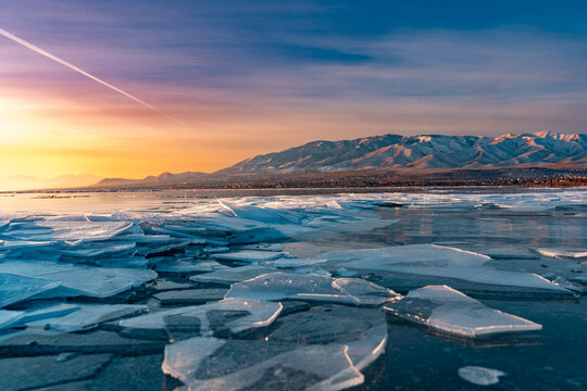 View of ice shove pile along the shoreline of Utah Lake at sunrise with snow-capped mountains in the background under a colorful sky in Saratoga Springs, Utah, United States.