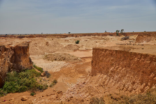 View of the arid landscape and reddish soil at a quarry site with dry cracked earth and sparse vegetation in Kuru, Plateau, Nigeria.