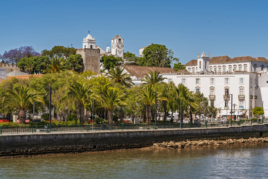 View of the historic town of Tavira with its white buildings, clock tower, and palm trees along the Gilao River in Tavira, Faro District, Portugal.