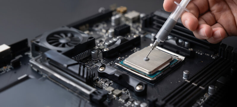 Professional technician uses a syringe to carefully apply a small drop of grey thermal paste onto the metal surface of a computer CPU to ensure efficient heat transfer and cooling for the system