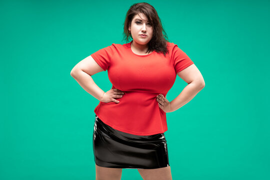Plus size fashion model in red blouse and black skirt, fat woman on green background, body positive concept