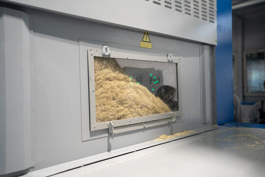 View of an industrial machine processing fibrous material visible through a glass window in a factory setting in Berlin, Berlin, Germany.