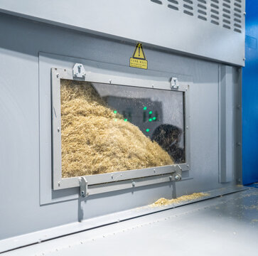 View of industrial machinery with a glass window showing processed fibrous biomass material inside a factory setting in Berlin, Berlin, Germany.