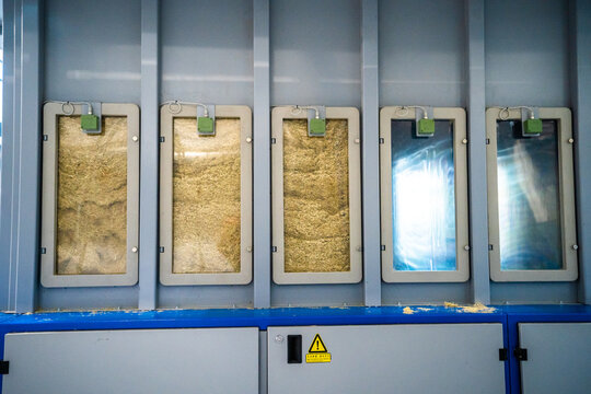 View of industrial biomass processing machinery featuring five vertical glass compartments filled with wood chips and a safety warning sign in Berlin, Berlin, Germany.