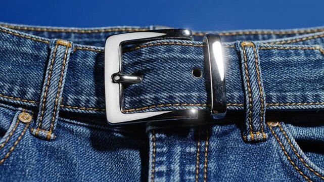 Close-up of a silver buckle on blue denim jeans with a textured background and warm stitching details