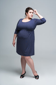 Plus size fashion model in blue polka dot dress, fat woman on gray background, body positive concept
