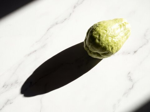 A single chayote on white marble casting one long hard shadow