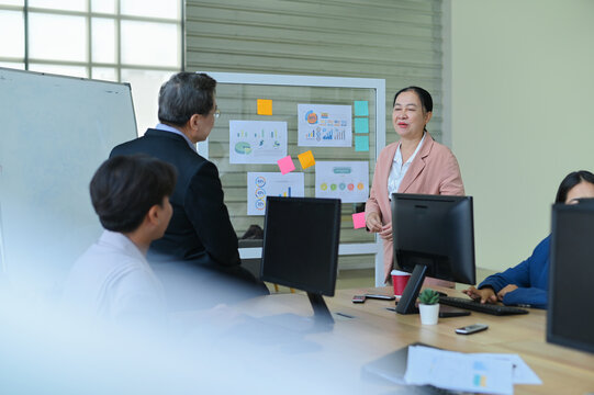 A vibrant office meeting scene showcasing a diverse group of professionals discussing projects with charts and post-it notes, emphasizing teamwork and collaboration.
