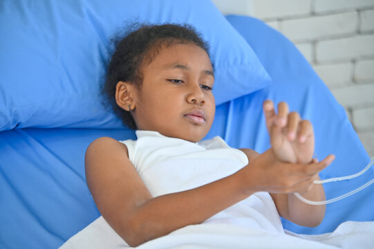 A young girl lies in a hospital bed, looking contemplative while interacting with medical equipment, evoking emotions of vulnerability and care.