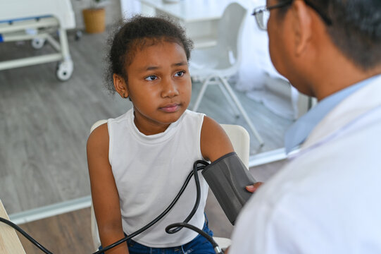 A young girl receives a blood pressure check from a healthcare professional in a modern medical setting, promoting the importance of health monitoring.