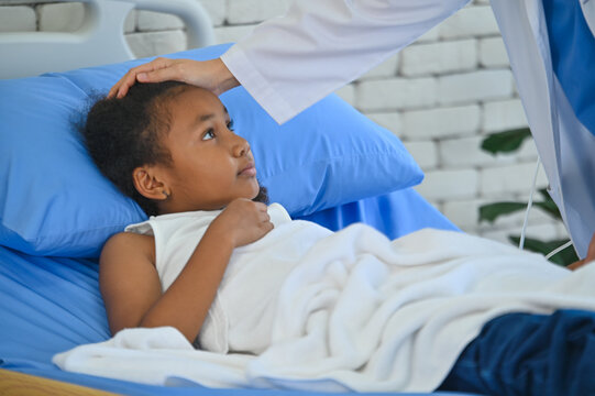 A young girl lies in a hospital bed, looking up with concern as a caregiver gently checks her temperature, highlighting the importance of health care for children.