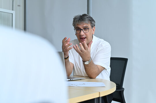 An engaging business meeting scene with a middle-aged man passionately discussing ideas at a conference table, surrounded by attentive colleagues.