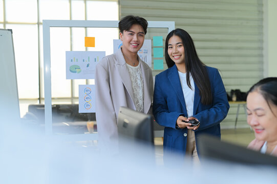 Two professionals smiling and collaborating in an office setting. They engage with their team and discuss creative ideas for future projects.