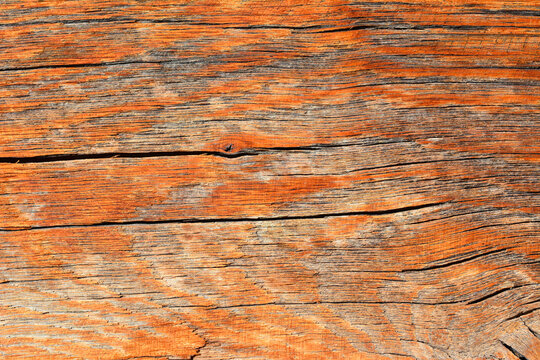 A close up horizontal shot of an old weathered oak wood board surface featuring deep rustic cracks and natural grain textures.