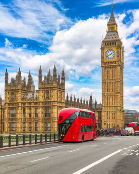 View of the iconic Big Ben clock tower and the Palace of Westminster with a red double-decker bus driving on the street in London, England, United Kingdom.