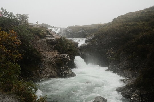 View of the cascading waterfalls at the Fairy Pools surrounded by rugged rocky terrain and misty hills in Isle of Skye, Scotland, United Kingdom.