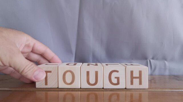 motivational word Tough, laying out by hand from letters on wooden cubes, slow motion

